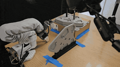 A robot arm executing a learned policy on real hardware, aligning and inserting a metal plate onto a fixture